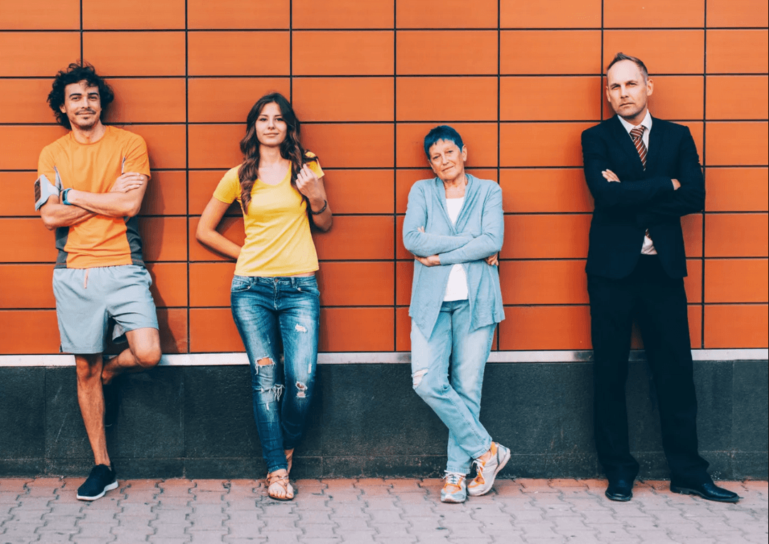 Four adults from different generations standing against an orange wall.