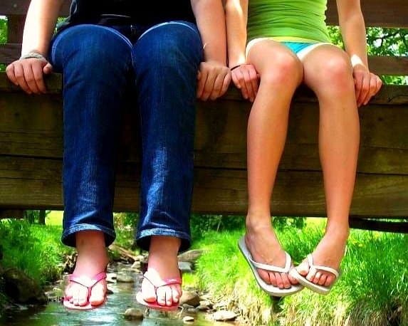 An adult and child sitting side by side on a wooden bridge.