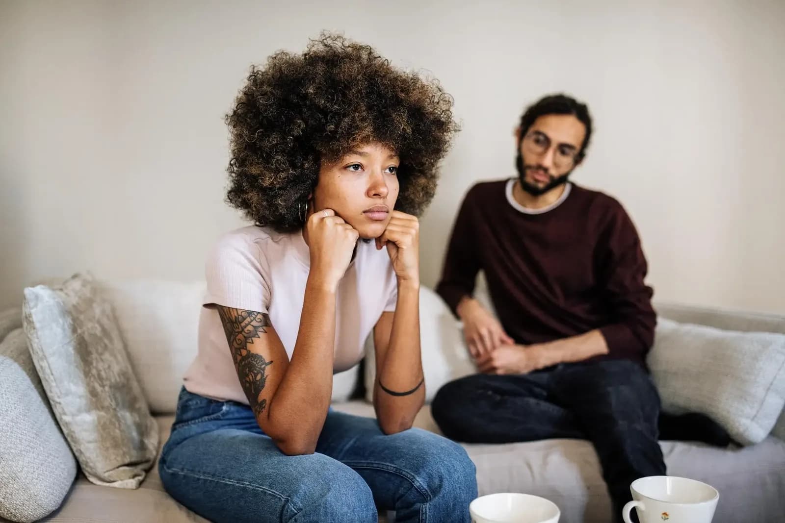 Woman resting her chin on her hands and looking away while a man sits behind her on a sofa.