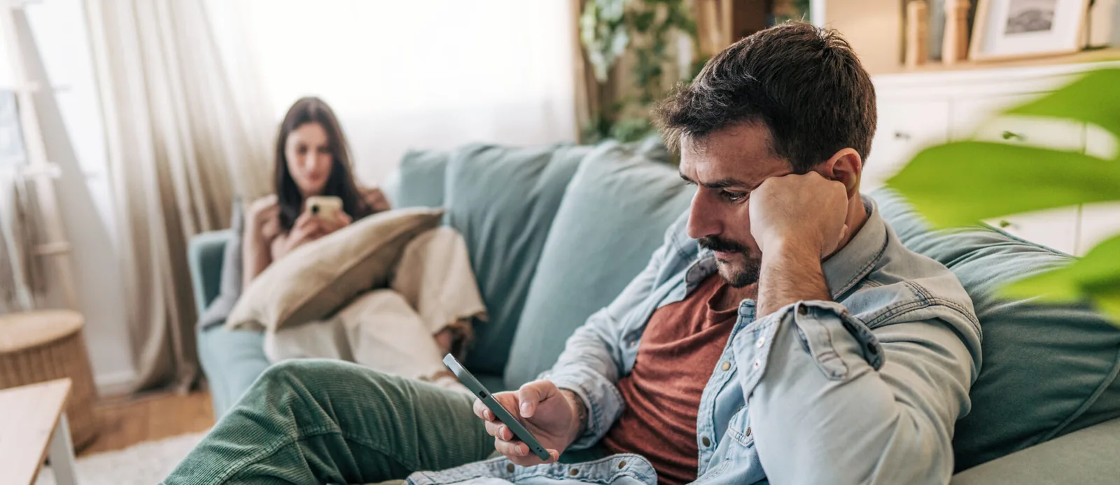 Man and woman sitting apart on a sofa, each looking at a phone.